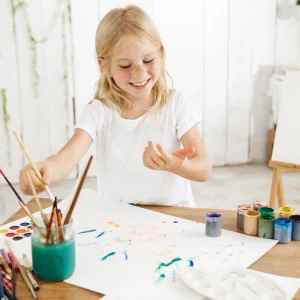 having-fun-joyful-smiling-with-teeth-blonde-seven-year-old-girl-dripping-paint-white-sheet-paper-lying-table-creative-child-having-fun-enjoying-painting (1)